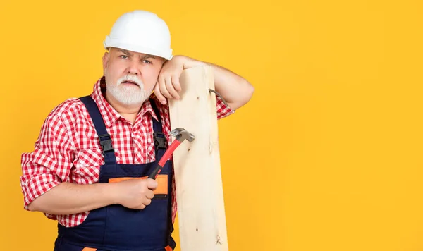 Müder alter Mann Holzarbeiter mit Helm auf gelbem Hintergrund — Stockfoto