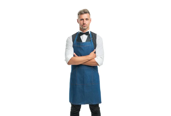 Fiducioso uomo in grembiule e arco tenendo le braccia incrociate isolato su bianco, cameriere. — Foto Stock