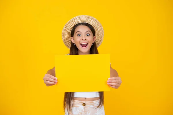 Surprised teen girl hold empty advertisement paper with copy space on yellow background — 스톡 사진