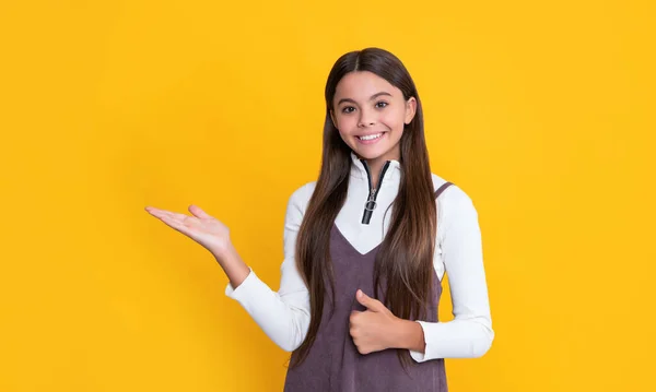 Positive child with long hair on yellow background. presenting product — Stockfoto