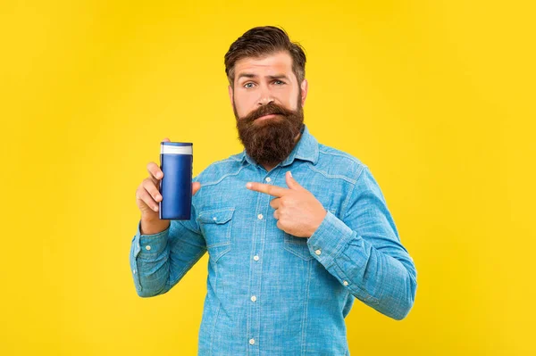Confused brutal bearded man point finger on shampoo bottle on yellow background, skincare — Foto Stock
