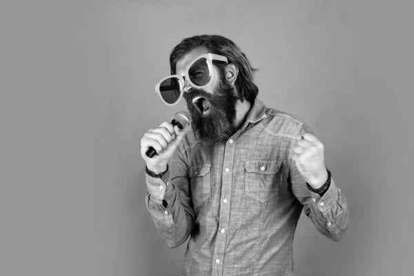 Mature bearded guy has long hair wearing party glasses and singing in mic, party — Stock Photo, Image