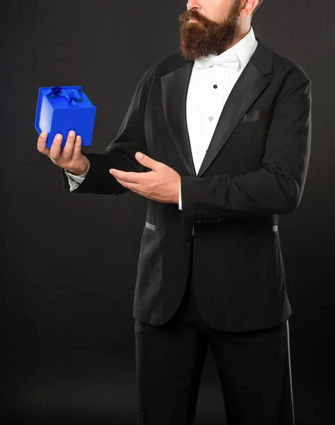 Copped man in tuxedo bow tie formalwear on black background presenting box. shopping sale — Stockfoto