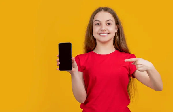 Happy child pointing finger on smartphone on yellow background — ストック写真
