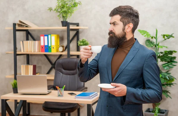 Уверенный жестокий генеральный директор в деловом костюме имеет перерыв на обед с чашкой кофе в офисе, бизнес — стоковое фото