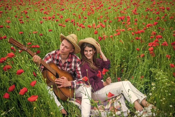 Ρομαντικό ζευγάρι που παίζει κιθάρα σε ένα πεδίο με κόκκινα λουλούδια, καλοκαιρινές διακοπές — Φωτογραφία Αρχείου