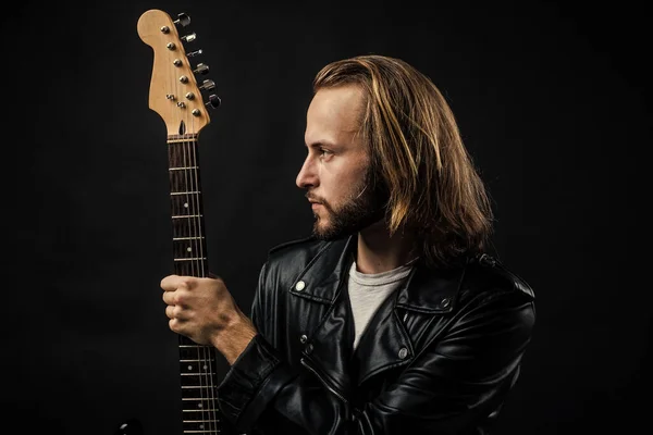 bearded rock musician holding electric guitar neck in leather jacket, rock music
