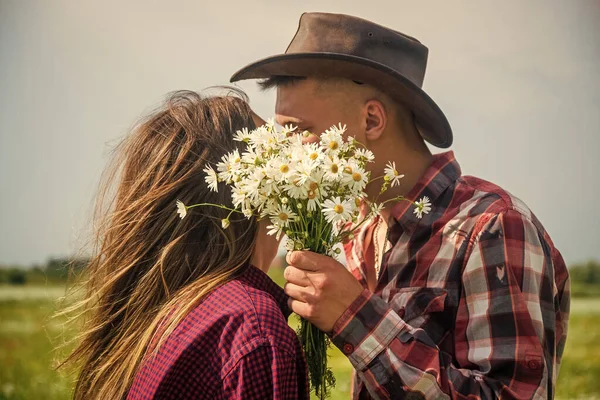 Par kär i man och kvinna kysser bakom tusensköna bukett i kamomill blomma fält, romantik. — Stockfoto