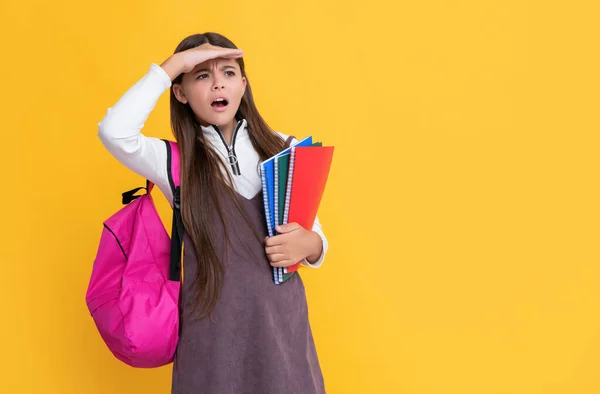 Překvapené dítě se školní batoh a sešit na žlutém pozadí — Stock fotografie