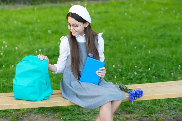 Happy child in glasses relax on park bench with book and backpack — стоковое фото