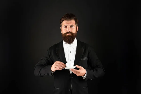 Serious man in tuxedo bow tie with coffee cup. gentleman drink coffee on black background. — Fotografia de Stock