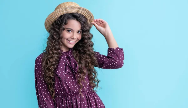 Lächelndes Kind mit Strohhut und langen brünetten lockigen Haaren auf blauem Hintergrund — Stockfoto