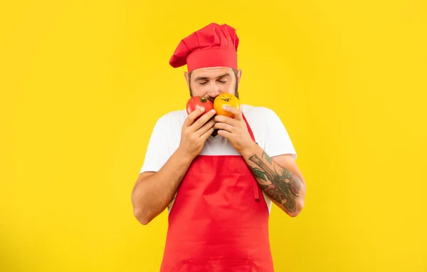 Homme sérieux dans tablier de cuisine et toque sentant les tomates avec les yeux fermés fond jaune, cuisinier — Photo