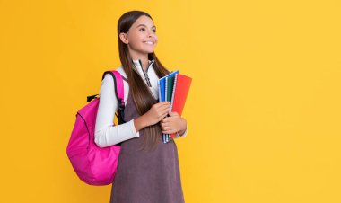 cheerful child with school backpack and workbook on yellow background
