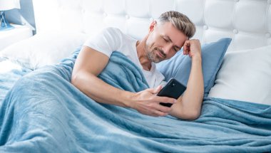 Yatakta neşeli olgun bir adam telefonda konuşuyor.