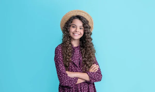 Enfant gai en chapeau de paille avec de longs cheveux bouclés brune sur fond bleu — Photo