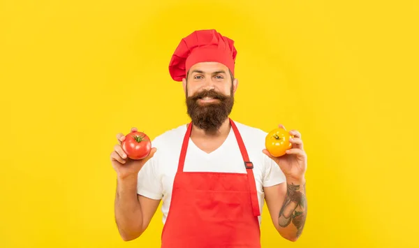 Happy man in apron and toque holding red and yellow tomatoes yellow background, cook — Stock Fotó