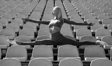 Sportif kadın ikiye bölünmüş. Stadyum spor salonunda esnek bir kadın. Bayan antrenör esneme egzersizi yapıyor. Yoga hocası. Spor başarısı. Esneklik kavramı. Fitness sporu modası. sağlıklı beslenme