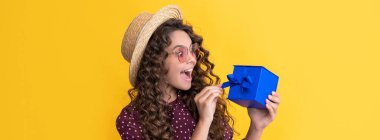 Kıvırcık saçlı hayret bir çocuk sarı arka planda hediye kutusunu tutuyor.