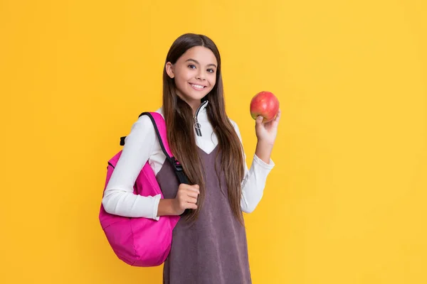Cheerful child with school backpack and apple on yellow background — Stockfoto