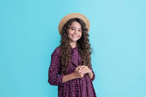 Lächelndes Kind mit Strohhut und langen brünetten lockigen Haaren auf blauem Hintergrund — Stockfoto
