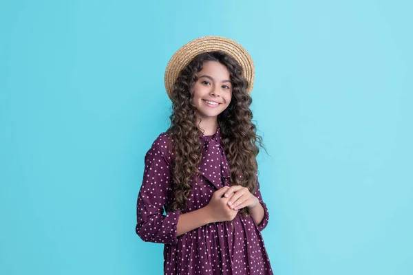 Enfant souriant en chapeau de paille avec de longs cheveux bouclés bruns sur fond bleu — Photo