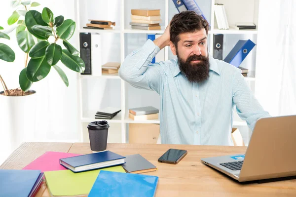 Zmatený podnikatel škrábání hlavy při práci na notebooku v kanceláři, zmatek — Stock fotografie