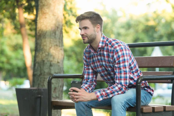 Jeune homme en chemise à carreaux avec tasse de café sur banc de parc — Photo