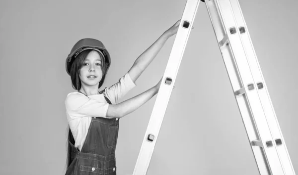 Ребенок на лестнице носит каску. строитель на стройке. инженер. архитектор в мастерской. ремонт и ремонт. девушка-подросток в шлеме и бойлерском костюме на стремянке — стоковое фото