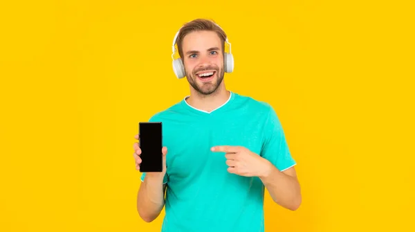 Teléfono que siempre te mantiene feliz. Un tipo feliz apuntando al teléfono móvil. Música smartphone — Foto de Stock