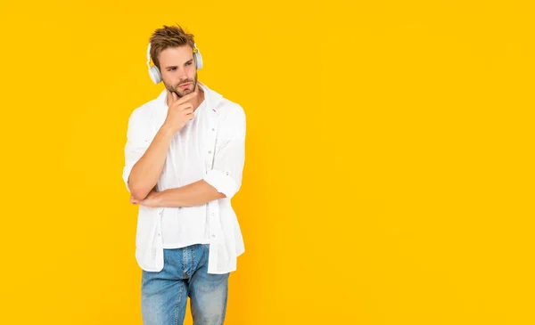 Nieogolony młody mężczyzna w słuchawkach na żółtym tle, nowoczesne urządzenie — Zdjęcie stockowe