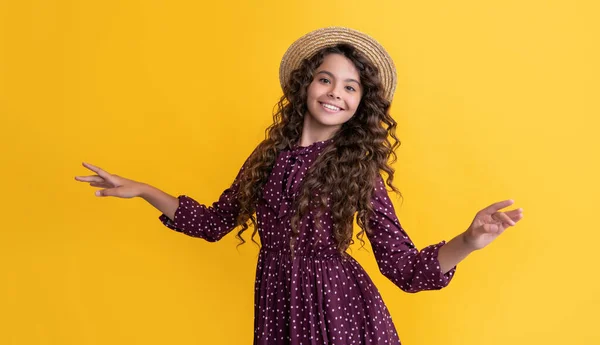 Lächelndes Kind mit Strohhut und langen brünetten lockigen Haaren auf gelbem Hintergrund — Stockfoto