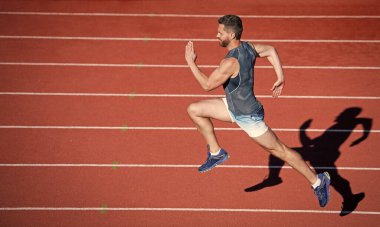 Enerjik atletik kaslı adam koşucu açık hava stadyumunda yarış pistinde koşuyor, acele et.