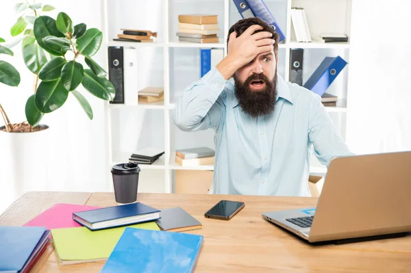 沮丧的男人紧紧抓住在办公室笔记本电脑上工作的头，沮丧不已 — 图库照片