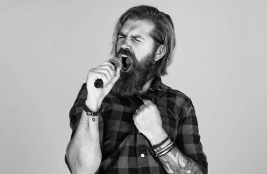 Sesini yükselt. Sıradan bir adam şarkı söylerken insani duygularını ifade eder. Mikrofonlu duygusal hipster. Mikrofonlu erkek şarkıcı. Karaoke konsepti. Kareli gömlekli sakallı adam şarkı söylüyor.