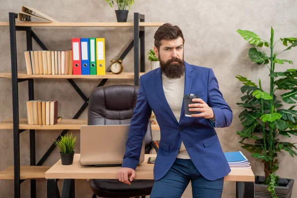 Серьезный работник в костюме пьет чай или кофе, работает в офисе, перерыв — стоковое фото