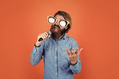 Bıyıklı komik sakallı vahşi adam parti gözlüğü takıyor ve mikrofonda şarkı söylüyor.