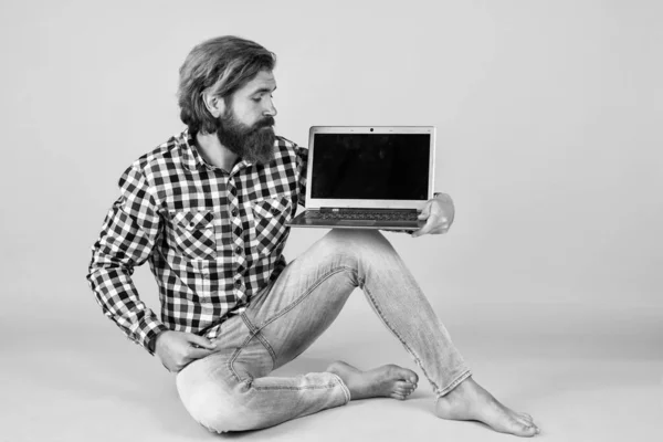 Hombre barbudo brutal usar camisa a cuadros con barba exuberante y bigote trabajando en el ordenador portátil, nueva tecnología — Foto de Stock