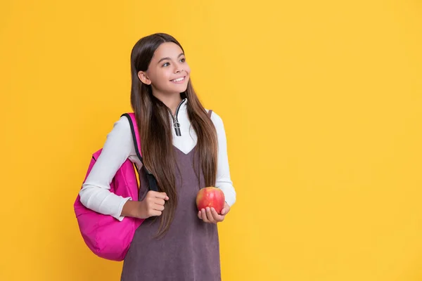 Pozitivní dítě se školní batoh a jablko na žlutém pozadí — Stock fotografie