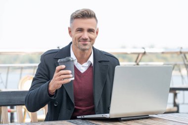 Bilgisayarda çalışıp açık kafede kahve içen mutlu bir iş adamı..