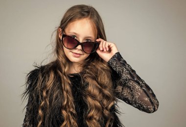 Moda gözlüğü takan şık bir çocuk. Mevsimlik sonbahar modası. Güneş gözlüklü genç kız. Mutlu çocukluk. Güzellik ve moda. Havalı olmak. Çocuğun uzun kıvırcık saç stili var. Boşluğu kopyala.