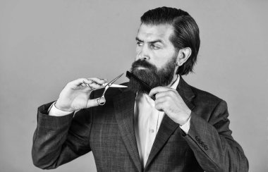 Hipster 'ın moda portresi. Uzun siyah sakallı ve bıyıklı yakışıklı adam saç fırçası ve makas tutuyor. Berber dükkanında saç ve sakal tımar etme ustası. Kuaför saç stili yapar..