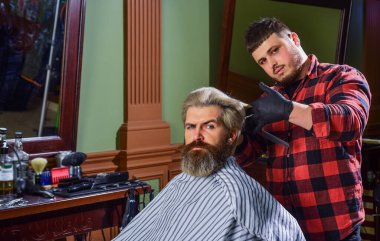 Moda ve güzellik. Profesyonel kuaförlük işi. Yaşam tarzı. Usta berber saç stilini ve saç stilini kurutma makinesiyle yapıyor. Berber dükkanı. Genç hippi sakallı adam berber dükkanında saçını kesiyor..