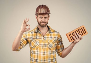 Profesyonel duvar ustası iyi bir jest yaptı. İnşaat mühendisi. İşçi ya da işçi günü. Tuğlalı bir işçi. Adam işçi üniforması giyiyor. Kasklı yakışıklı bir müteahhit. Olgun adam kareli gömlek giyer..