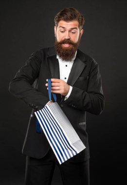 Smokinli, papyonlu, siyah arkaplanlı, erkek erkeğe alışveriş torbası takan meraklı bir adam..