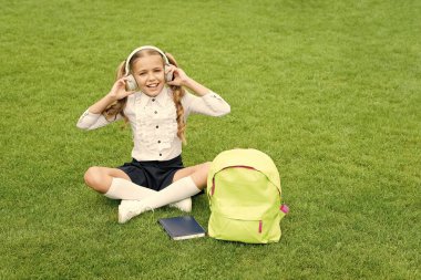 Mutlu genç kız müzik dinliyor okuldan sonra yeşil çimlerde oturuyor, kulaklık takıyor..