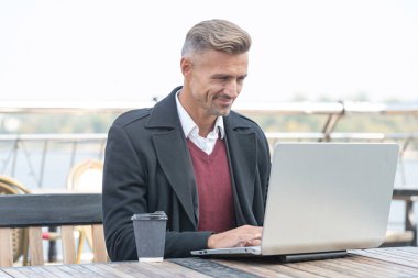 Serbest çalışan mutlu bir adam açık kafede dizüstü bilgisayarda çalışıyor..