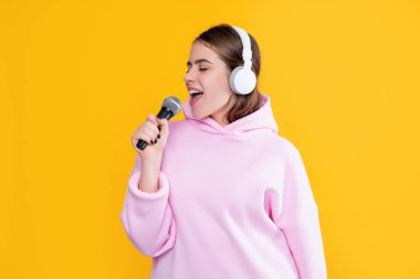 Sarı arka planda mikrofonu olan kulaklıklı mutlu genç bir kadın..