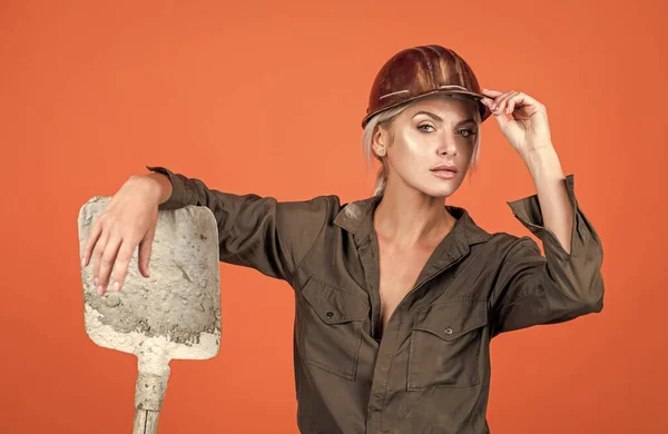 a bit tired. building and construction. lady architect worker. engineer on orange background. foreman girl wear safety hardhat. labor day. woman in boilersuit and helmet. female builder hold shovel.