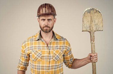 İnşaat kaskı ve kareli gömlekli yakışıklı işçi inşaat alanında kürekle, sanayiyle....